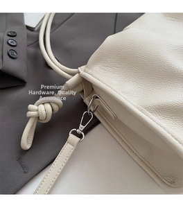 Close-up of beige lychee grain leather bag with silver metal hook and knot detail