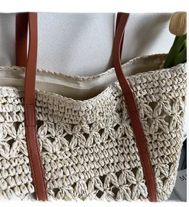 Detail of hollow woven straw tote bag featuring premium brown leather shoulder straps