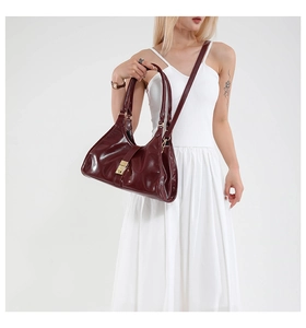 Deep red patent leather trapezoid handbag with gold metal clasp on a white dress