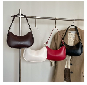 Minimalist crescent underarm bags displayed in four colors on a modern clothing rack
