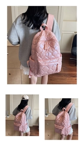 Detail of pink heart-quilted puffer backpack featuring woven zipper pulls and padded straps