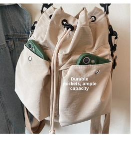 Detail of beige nylon bucket bag featuring large utility front pockets for mobile phones