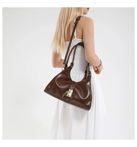 Side view of dark brown glossy hobo bag with adjustable strap on a white dress model