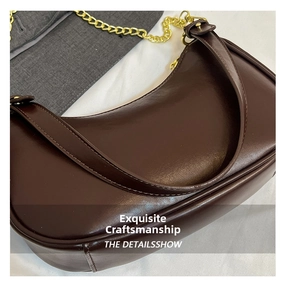 Detail of dark brown crescent bag with stitching, gold chain, and faux leather texture