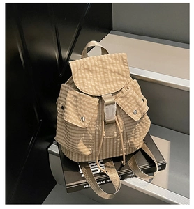 Detail of plaid canvas backpack featuring drawstring closure and front metallic snap pockets