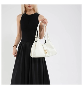 Détail d'un sac à main en cuir verni blanc avec fermoir doré sur une tenue noire