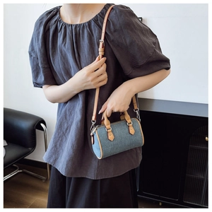 Detail of a mini denim pillow bag with leather trim and adjustable shoulder strap