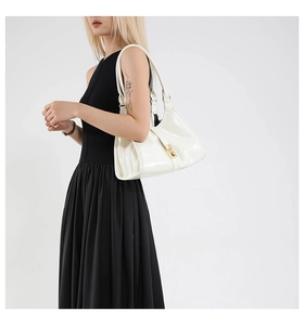 Side view of model wearing white patent leather handbag with golden lock buckle detail
