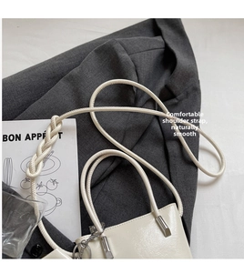 Close-up of cream bucket bag showing glossy leather texture and braided strap detail