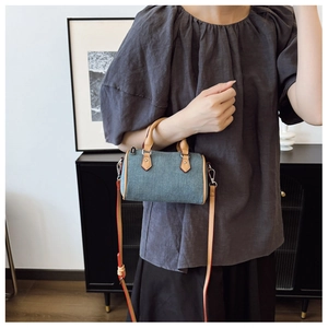 Detailed close-up of a blue denim mini Boston bag with tan leather handles and red edges