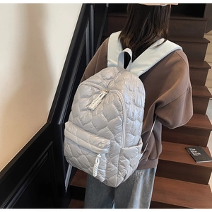 Close-up of light grey quilted backpack with heart patterns and woven zipper details