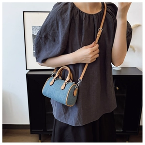 Detail view of light blue denim pillow bag with brown leather handles and silver hardware