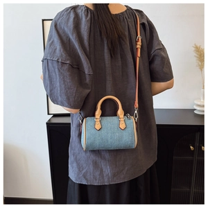Mini denim pillow bag with leather handles shown as a shoulder bag on a model
