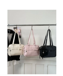 Three stylish bow shoulder bags in white, pink and black hanging on a metal rack