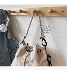 Close-up of cream nylon bucket bag with drawstring closure and black metal hardware