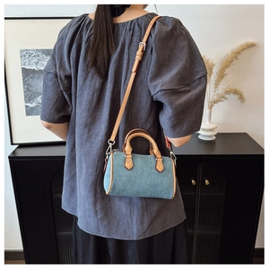 Detail showing small denim boston bag with brown leather handles worn by a model