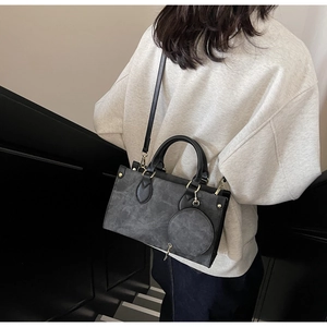 Rear view of a dark grey suede tote bag with black handles and a small round coin purse