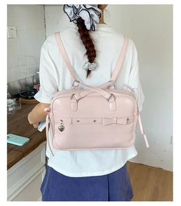 Pink JK uniform bag with bow details and silver heart charm shown in a backpack style