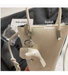 Detail of a beige leather bucket bag with fashion lettering and elephant charm accessory