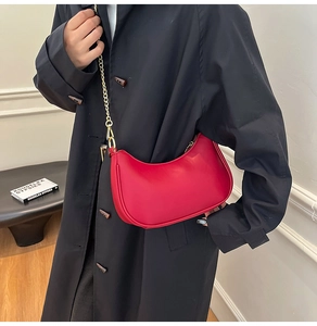 Red half-moon shoulder bag with gold chain strap shown on a black trench coat