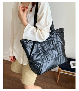 Close-up of quilted black puffer tote bag with side zipper pocket and brand embroidery