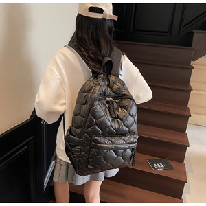 Detailed view of black quilted puffer backpack with wide shoulder straps on a wooden staircase