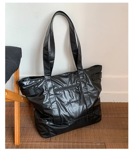 Detail of black glossy nylon tote bag featuring front zip pocket and script embroidery