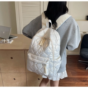 Detail of white quilted puffer backpack featuring soft padded fabric and front zipper pocket