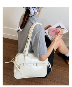 White JK style shoulder bag with bow and heart pendant shown on model in lifestyle setting