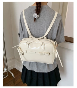 Detail of cream white faux leather backpack with decorative bow and silver heart pendant