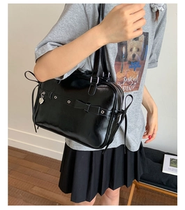 Detail of black glossy shoulder bag with bow decor and silver heart pendant charm