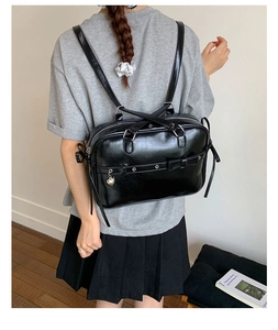 Detail of black glossy PU backpack with bow and heart charm in preppy style