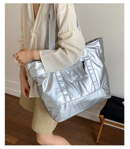 Detail of silver metallic tote bag featuring embroidered script and front zipper pocket