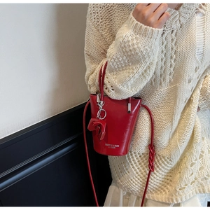 Detail view of a glossy red bucket bag with bow charm and leather strap on a model