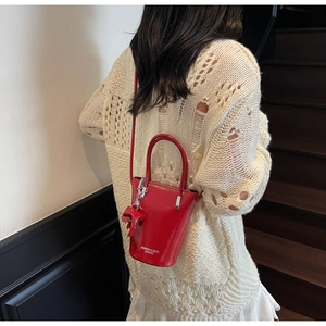 Detail of red shiny leather bucket bag with bow and text on cream knit sweater background
