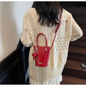 Detail of red leather bucket bag with woven knot strap and cute cartoon charm