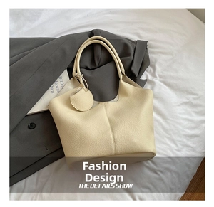 Detail of off-white tote bag with lychee texture leather and a circular charm