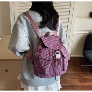 Detail eines lila karierten Rucksacks mit Klappenverschluss und kleinen Seitentaschen