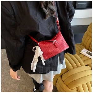 Détail du sac seau rouge tressé avec accessoires élégants en perles et dentelle