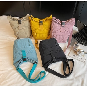 Detalle de bolsos bandolera de nailon de colores con cierre de hebilla en una cama blanca