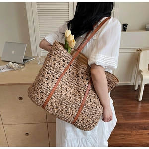Close-up of hand-woven straw tote bag with brown leather straps and hollow patterns