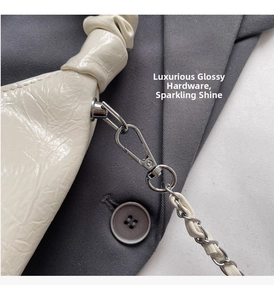 Detail of glossy pleated cream handbag with polished silver metal chain and lobster clasp