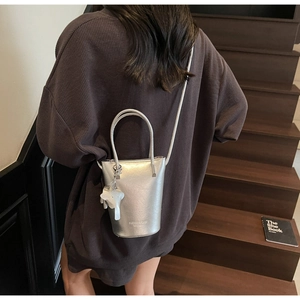 Detail of silver mini bucket bag with leather texture and white elephant charm accessory