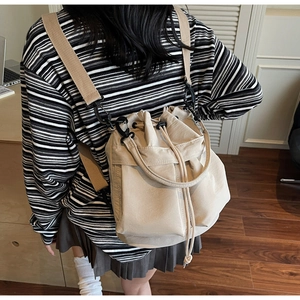 Beige drawstring bucket backpack worn on back showing adjustable straps and versatile style