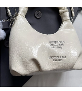 Close-up of white ruched leather bag with silver chain and decorative fur pompom