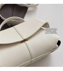 Close-up of litchi grain leather texture and gold buckle on a cream crossbody bag