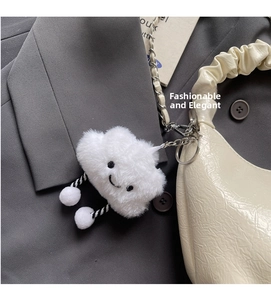 Detail of white plush cloud charm with embroidered face and metal chain on a handbag