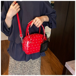 Detail shot of a red patent leather bowling bag with white heart patterns and top handle