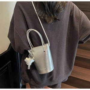 Silver bucket bag with metallic finish and elephant charm worn as a crossbody bag