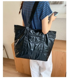 Detail of glossy black nylon tote bag showing zipper pocket and wide strap on model